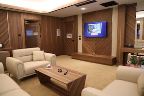 A modern hotel room with a wooden wall panel design, a flat-screen TV, a sofa, a coffee table, and a small seating area. - PL Managed By Dedeman (Istanbul)