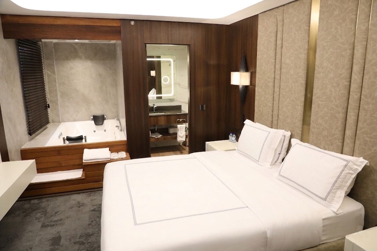 A modern hotel room with a large bed, a separate bathroom with a bathtub, and a vanity with a mirror.