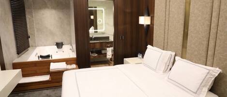 A modern hotel room with a large bed, a separate bathroom with a bathtub, and a vanity with a mirror.