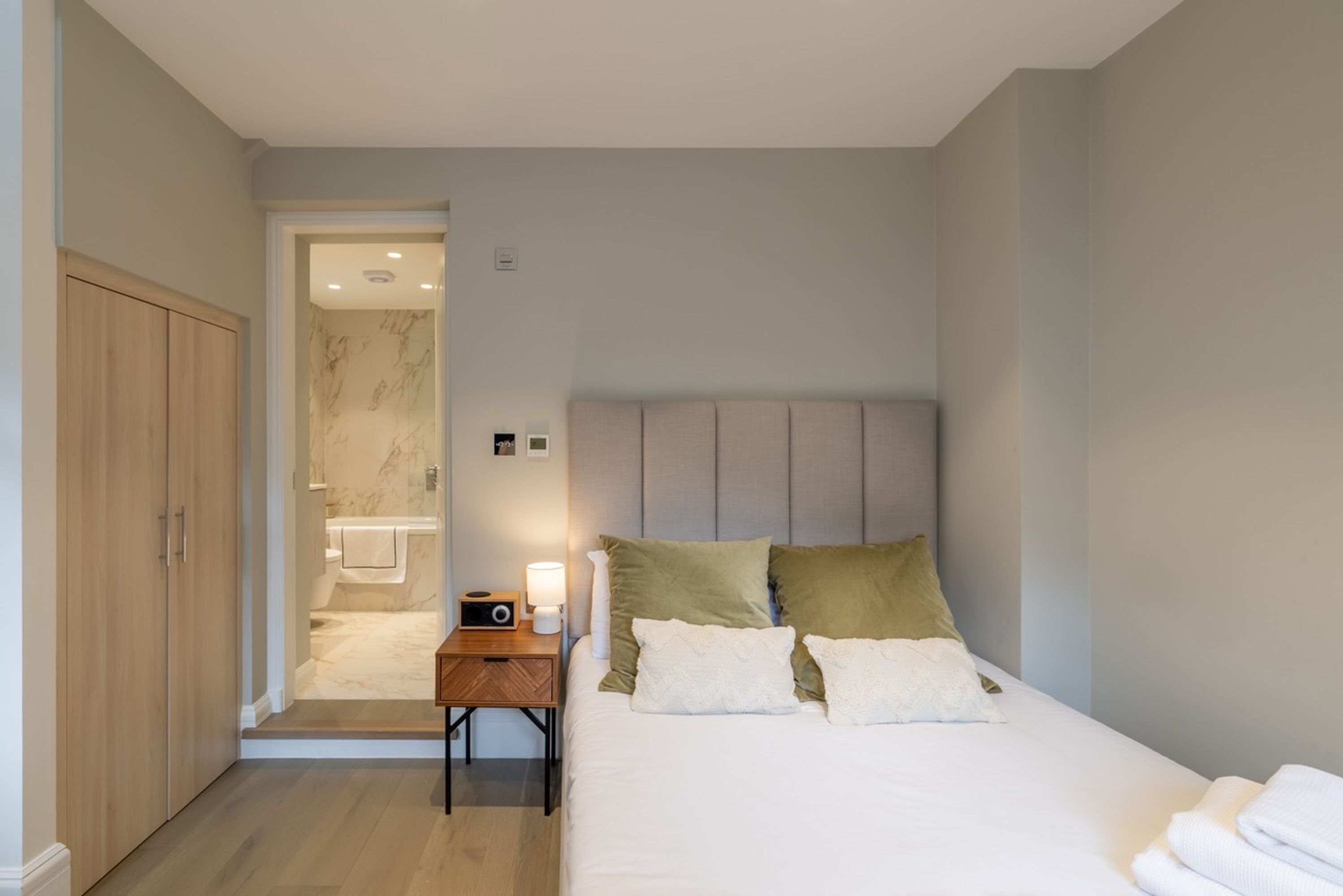 A hotel room with a bed, a nightstand, a wooden wardrobe, and a bathroom visible through an open door.