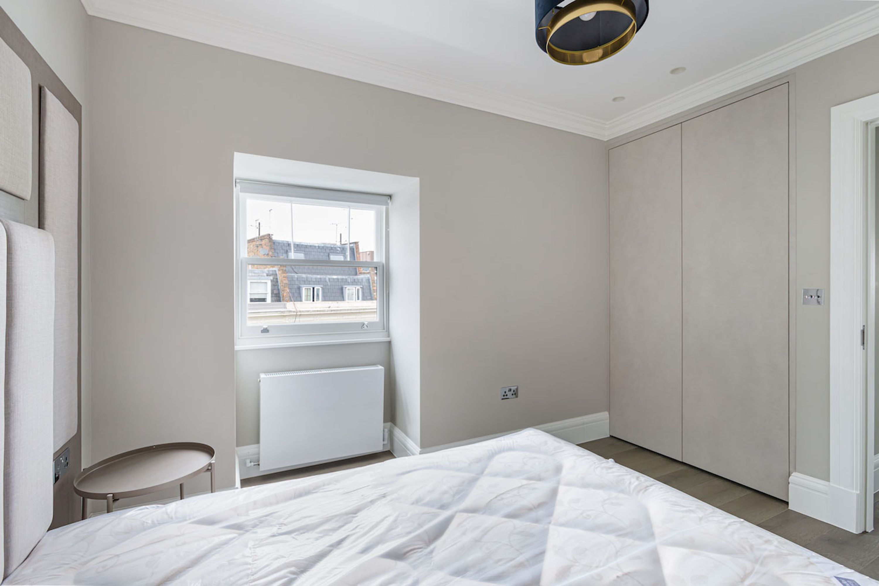 A bedroom with a bed, a window, a radiator, a wardrobe, and a ceiling light fixture.