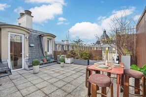 Een terras met een tafel voor twee personen, omringd door plantenpotten en een houten hek.