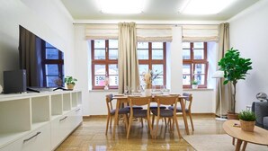Un salon moderne comprenant un coin repas, un téléviseur à écran plat et de grandes fenêtres avec des rideaux.