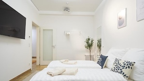 Une chambre d’hôtel avec deux lits, un téléviseur à écran plat, une plante et une porte donnant sur une autre chambre.