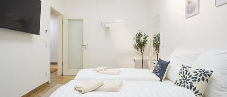 A hotel room with two beds, a flat-screen TV, a plant, and a door leading to another room.