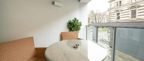 Un balcon agrémenté de meubles en osier, d’une table en verre et d’une plante en pot.