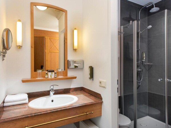 A bathroom with a wooden vanity, a large mirror, a white sink, and a glass-enclosed shower.