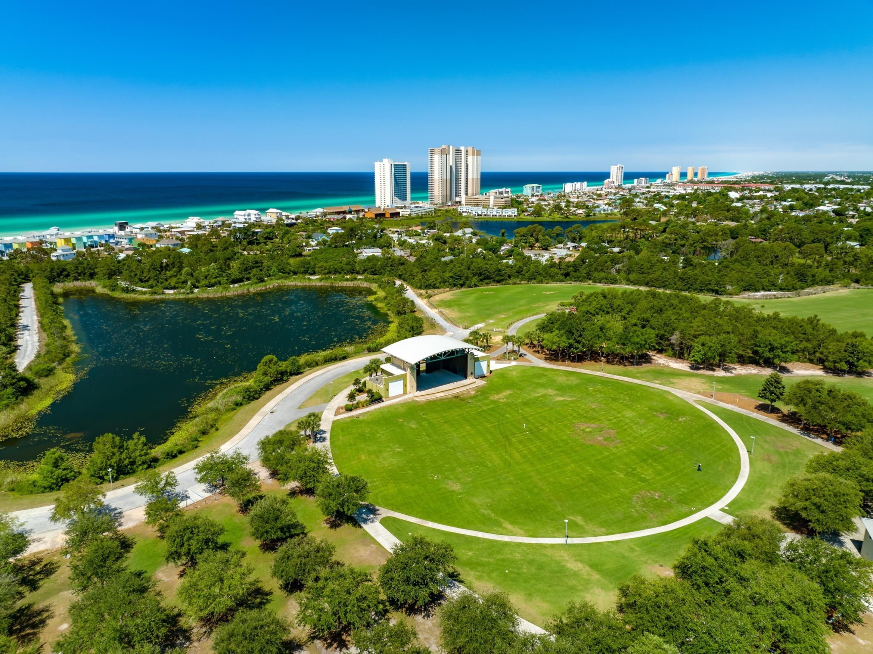 An aerial view of a park with a large green field, a lake, and a building with a white roof.