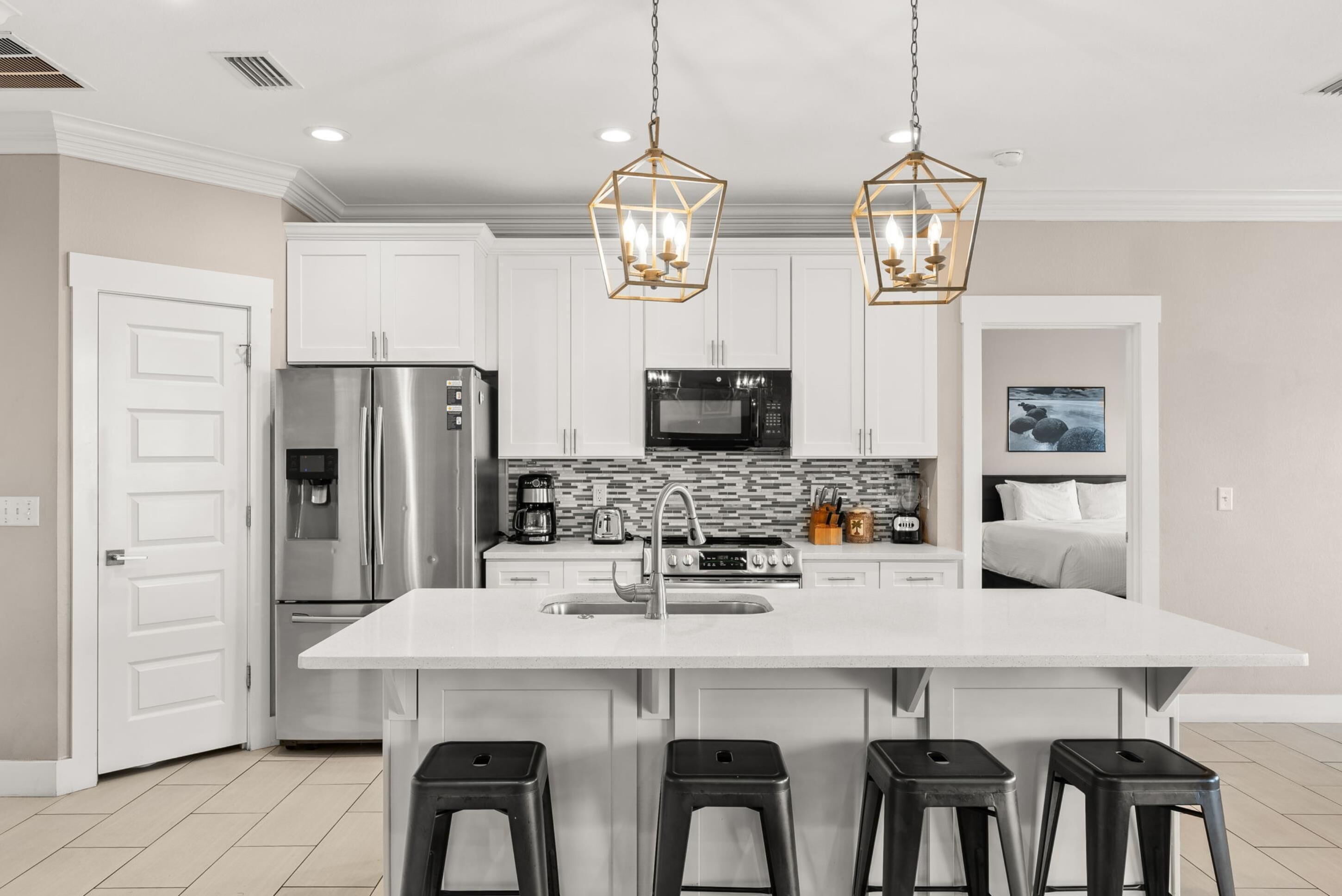 A modern kitchen with white cabinets, stainless steel appliances, a large island with bar stools, and pendant lighting.
