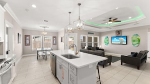 A spacious kitchen with a central island, a dining area, and a living room with a sofa and chairs. - Beach House - Beachside Sunrise (Panama City Beach)