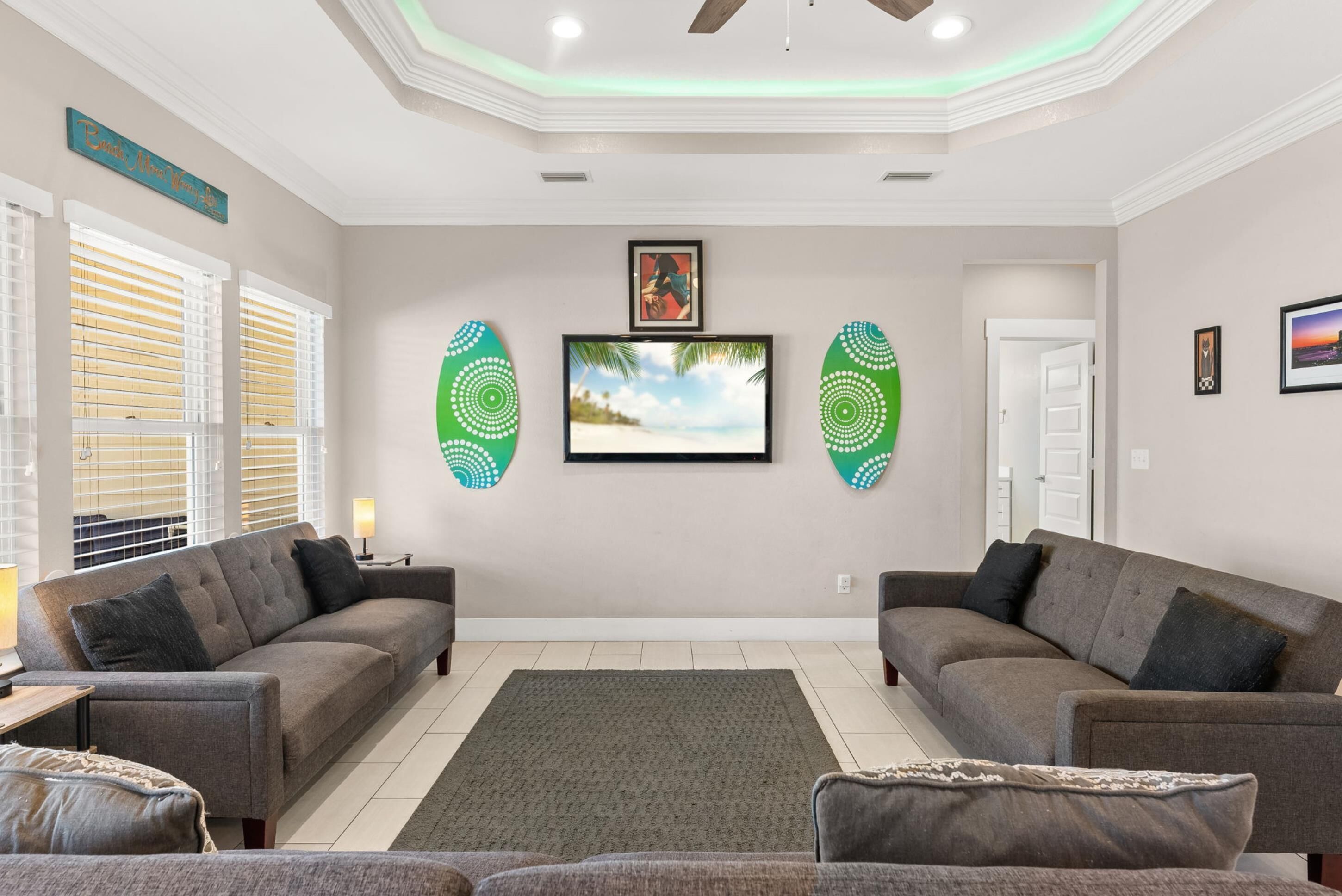 Una sala de estar con dos sofás, un televisor de pantalla plana, decoración en la pared y un ventilador de techo.