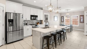 A modern kitchen with white cabinetry, stainless steel appliances, and a central island with bar stools. - Beach House - Beachside Sunrise (Panama City Beach)