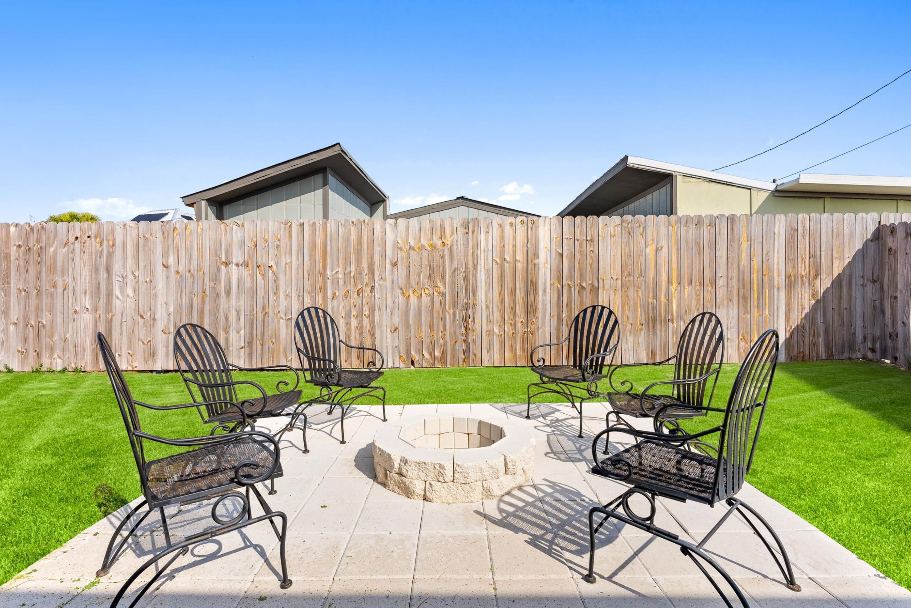 A backyard with a fire pit, four metal chairs, and a wooden fence.