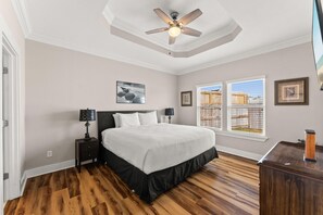 Un dormitorio con una cama, dos mesitas de noche, un ventilador de techo y una ventana con persianas.