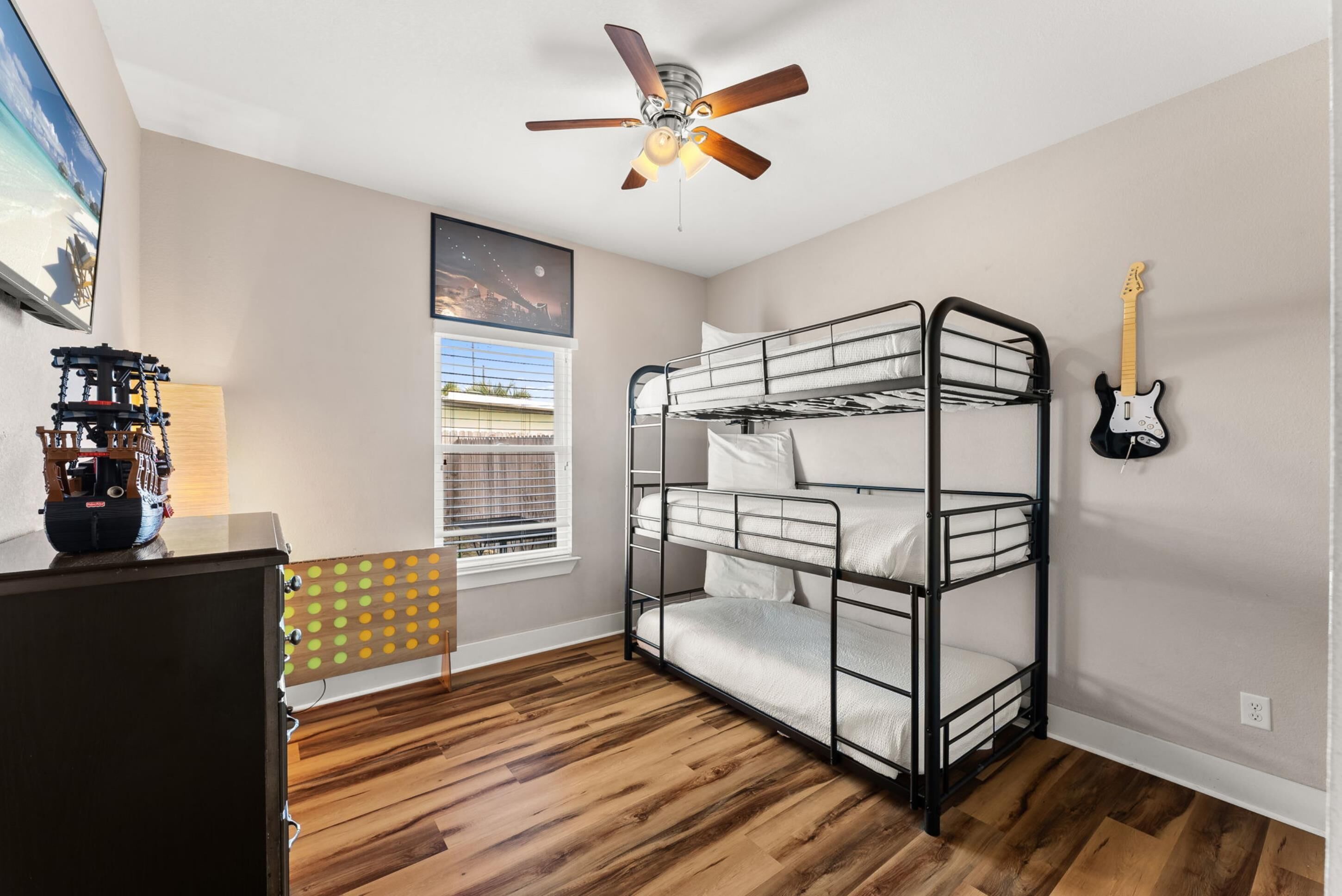 A bunk bed room with a ceiling fan, a guitar, and a window with blinds.