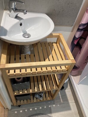 Ein Badezimmer mit weißem Waschbecken, einer Holzboden-Waschtischbank und einer Duschvorhang.