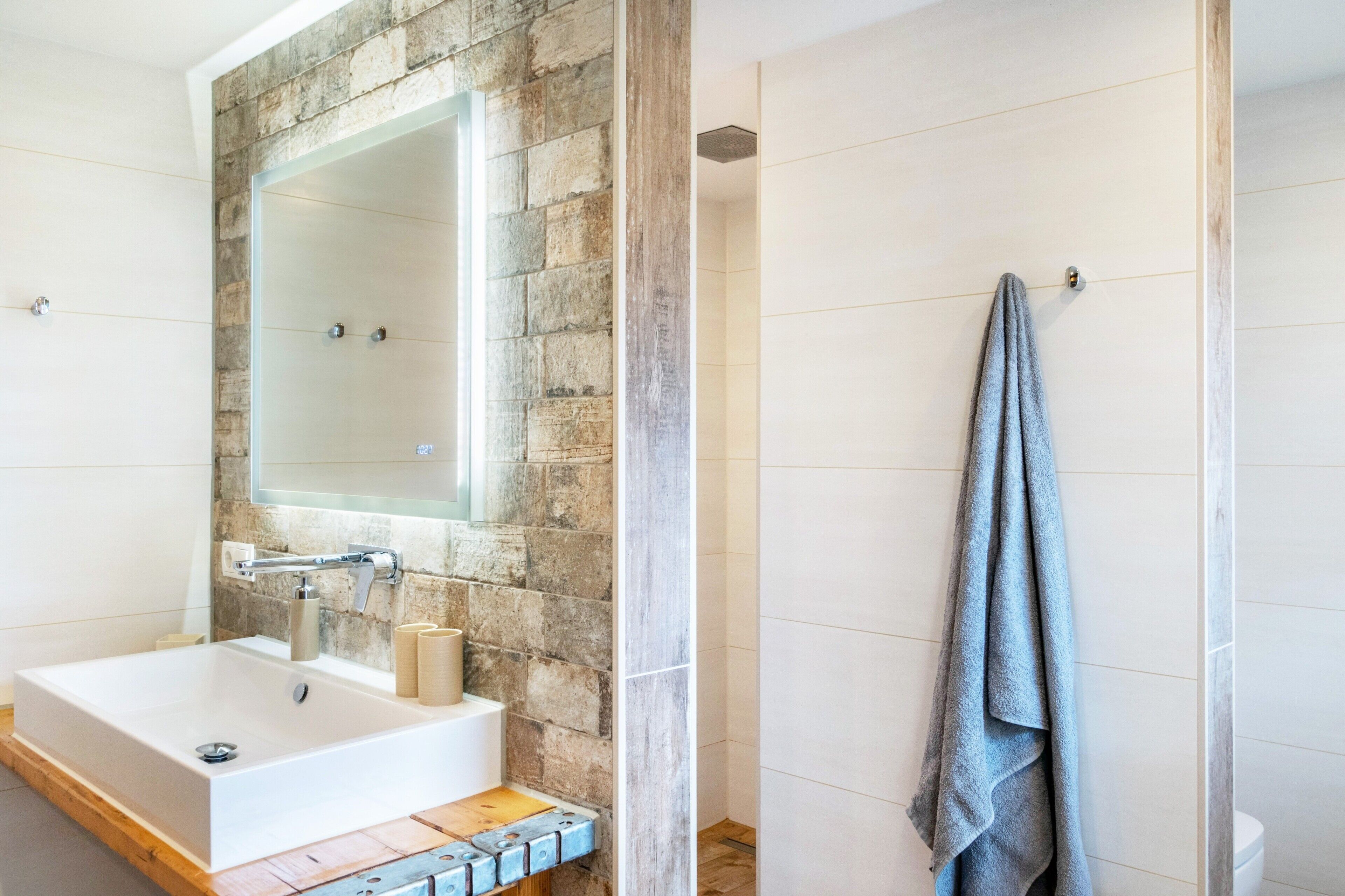 Ein Badezimmer mit Steinwand, großem Spiegel, Waschbecken und Handtuchhalter.