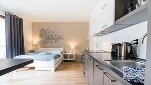 Een moderne hotelkamer met een bed, nachtkastje, en een kitchenette met een spoelbak en waterkoker.