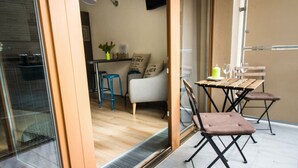 Een moderne woonruimte met een schuifdeur naar een balkon, een eettafel met stoelen, een bank en een plant in pot.