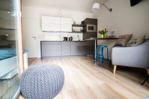 Una cocina moderna con armarios grises, un microondas y una cafetera. Hay un taburete azul y un sofá gris con cojines decorativos.