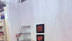Ett vardagsrum med en beige soffa, ett soffbord i genomskinligt glas och en vas med blommor. På väggen hänger två inramade konstverk, och det finns en hylla med dekorativa föremål.