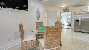 A modern kitchen with a large refrigerator, a dining table with wicker chairs, and a flat-screen TV mounted on the wall. - Clearwater Beach Home w/ Pool & Pool Table Room (Clearwater Beach)