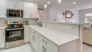 A modern kitchen with white cabinetry, stainless steel appliances, and pendant lighting. - Clearwater Beach Home w/ Pool & Pool Table Room (Clearwater Beach)