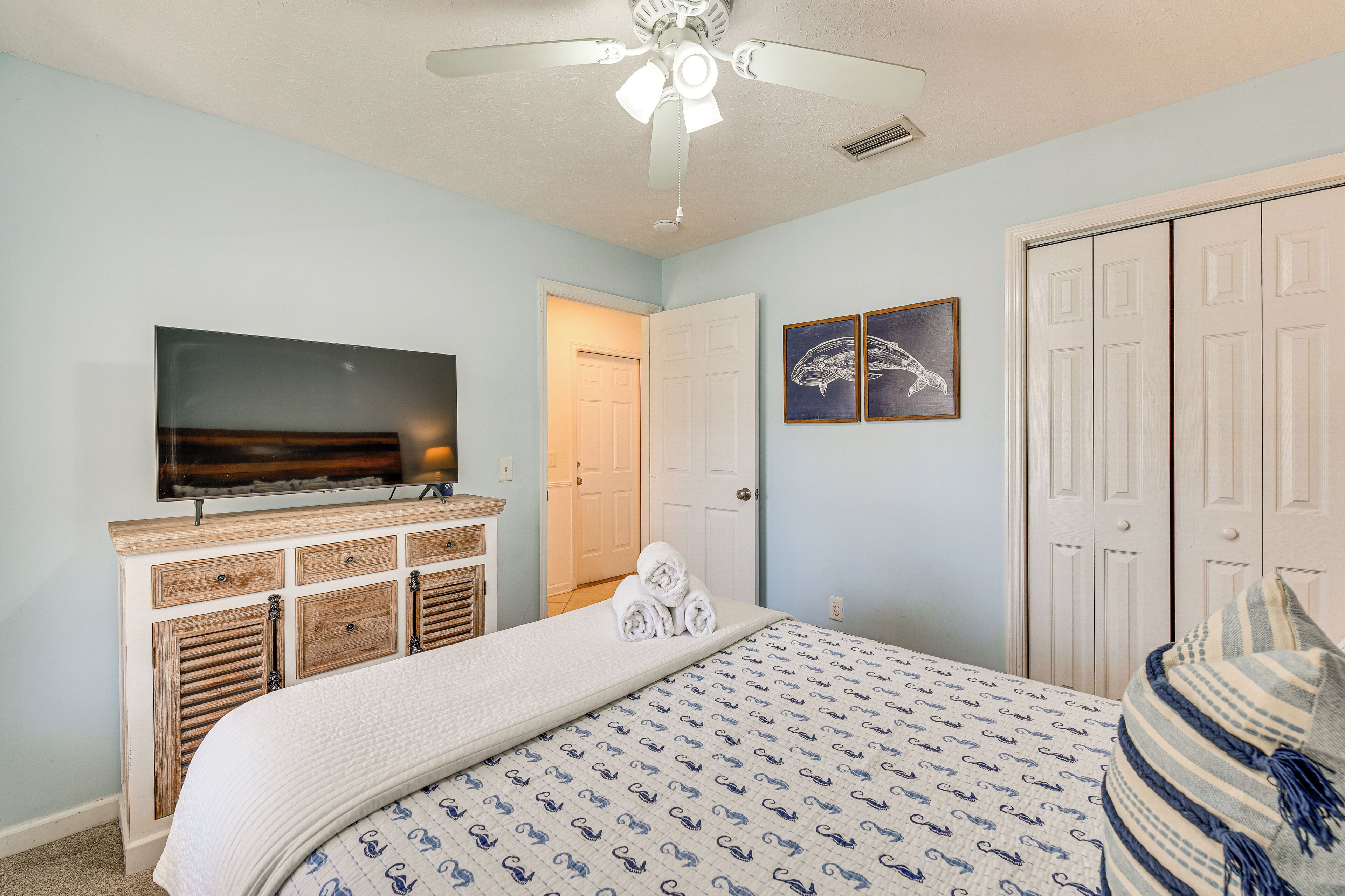 A bedroom with a bed, a television, a wardrobe, and a ceiling fan.