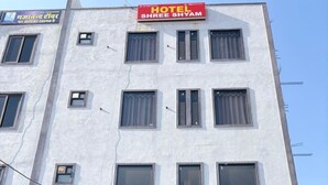 A hotel with a signboard reading "HOTEL SHREE SHYAM" and a contact number. There are multiple windows on the building, and a staircase leading to the entrance. - Hotel Shree Shyam and Restuarant (Jaipur)