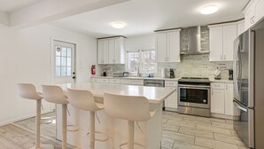 Une cuisine moderne avec des meubles blancs, un îlot central doté de tabourets, des appareils en acier inoxydable et un dosseret carrelé.