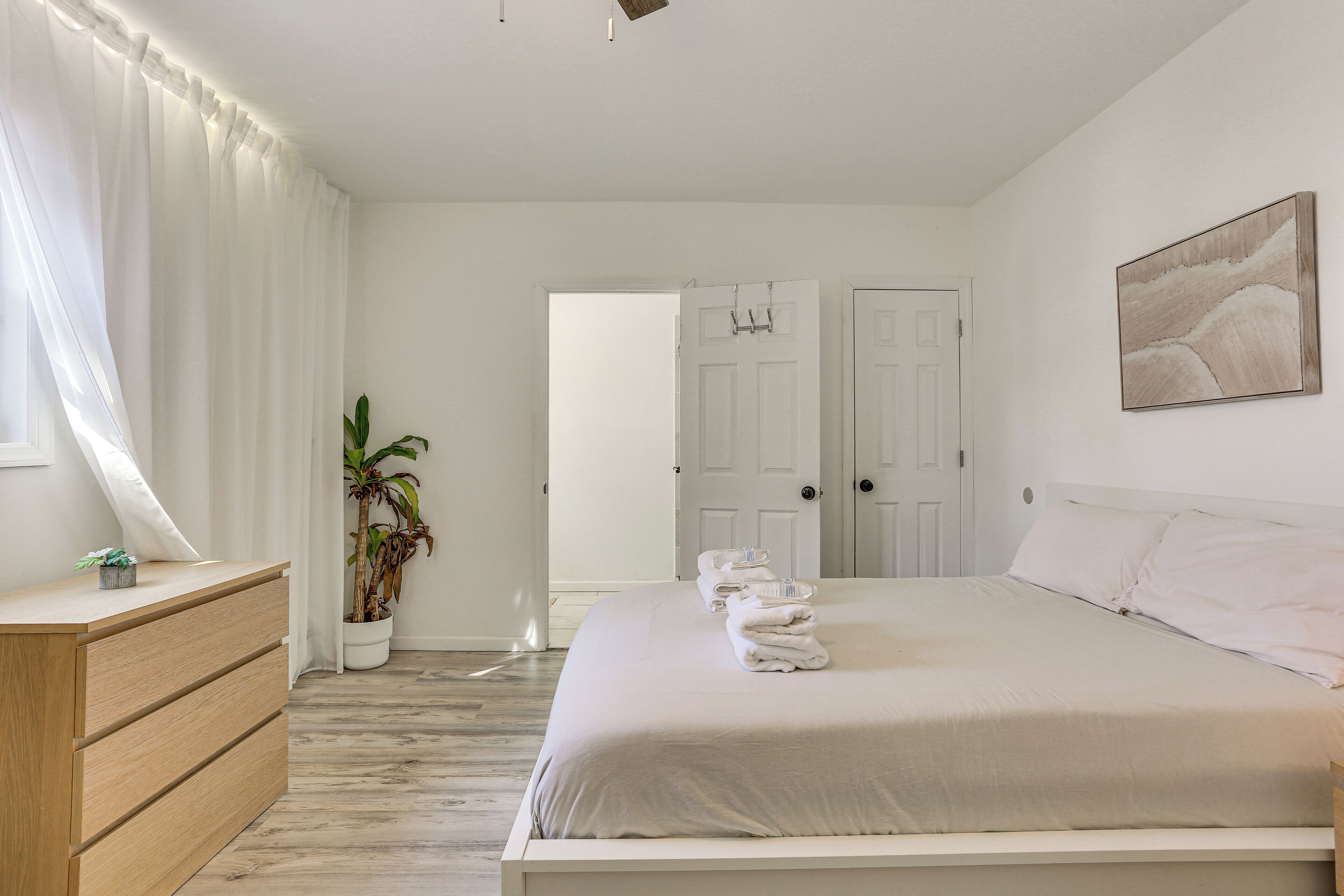 A bedroom with a bed, a dresser, a potted plant, and a door.