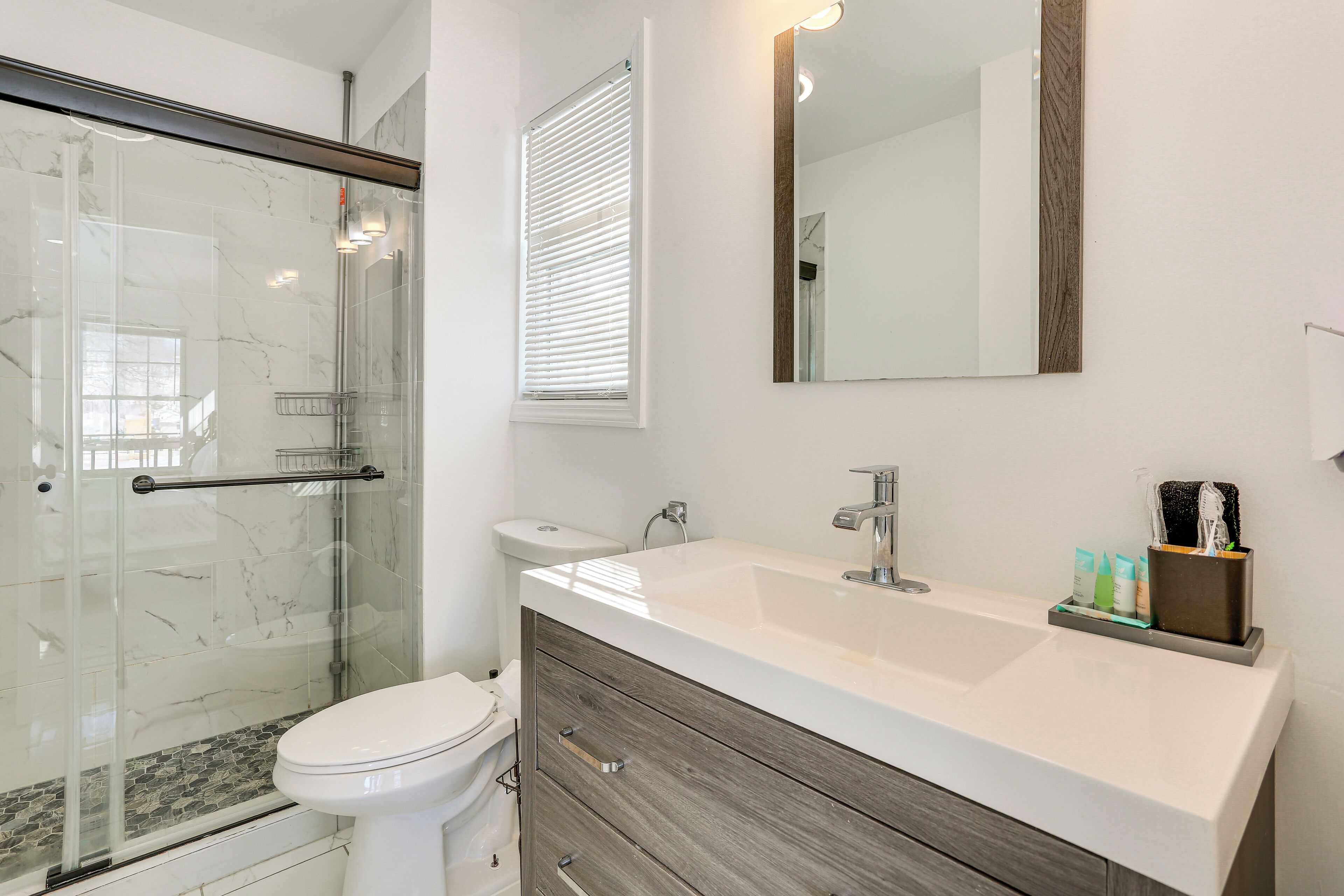 A modern bathroom with a glass shower enclosure, a white toilet, a vanity with a mirror, and toiletries.