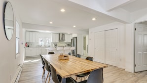 Un grand espace à manger avec une table et des chaises en bois, une cuisine à l’arrière-plan et un grand miroir sur le mur.