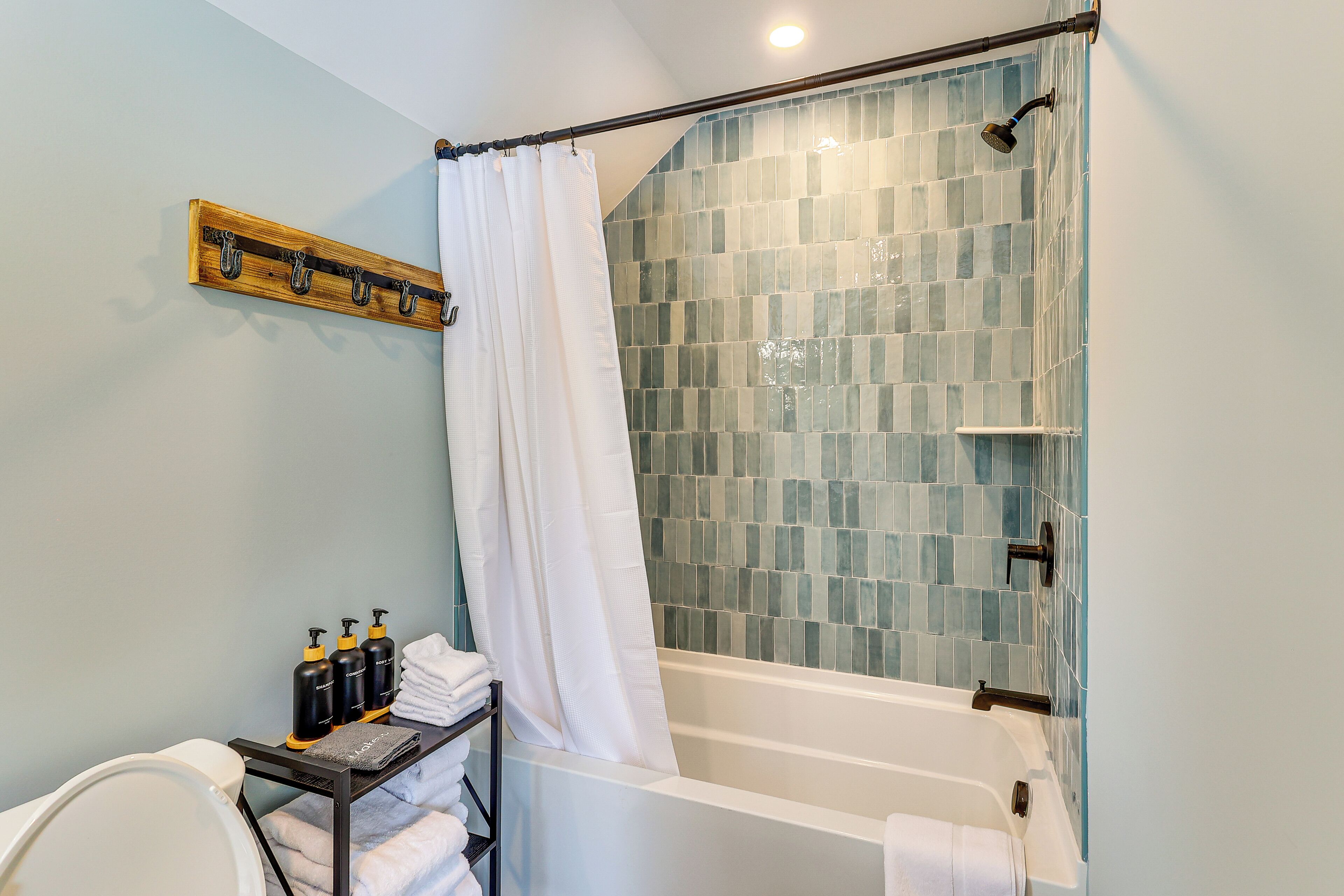 A bathroom with a shower, a bathtub, a towel rack, and toiletries.
