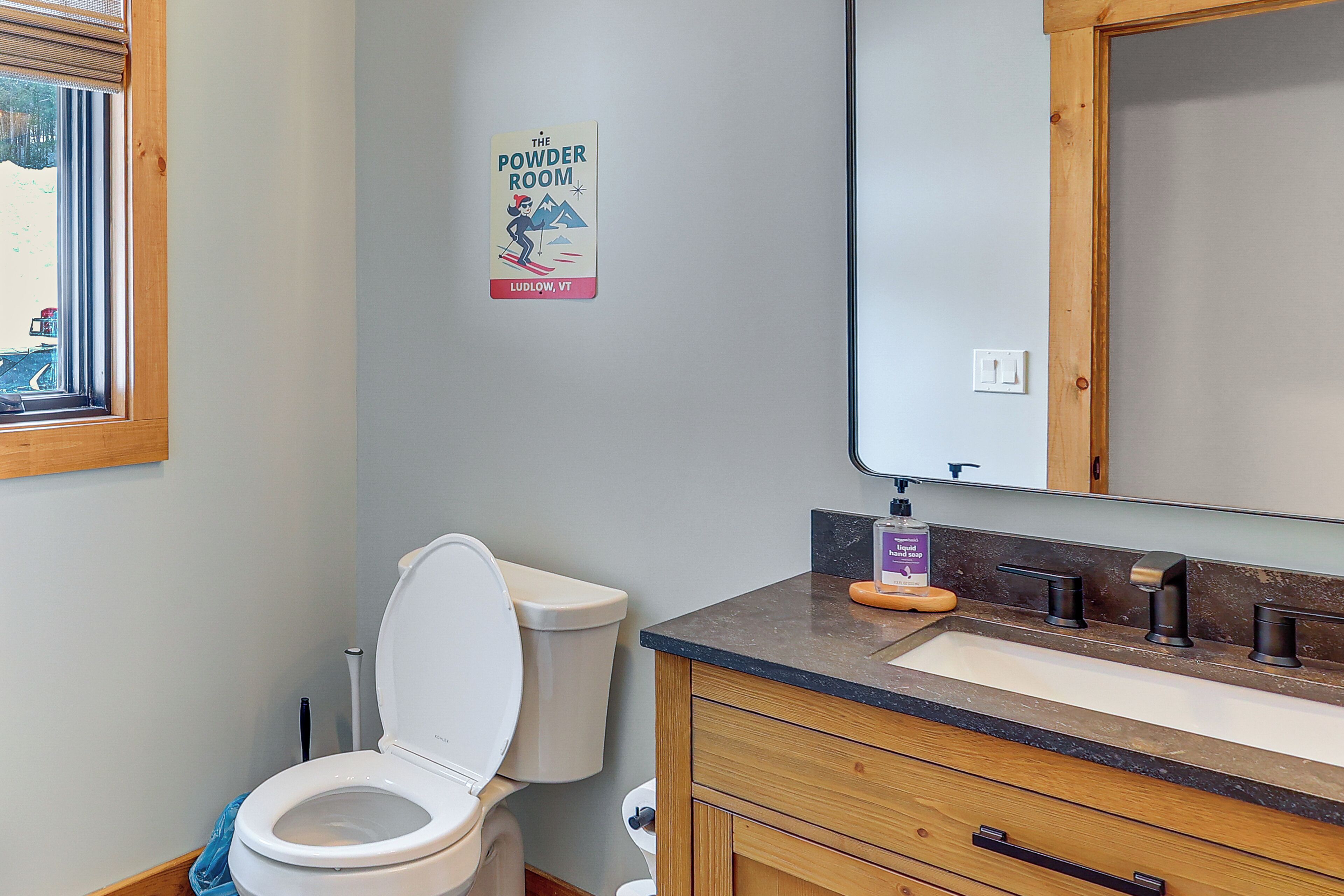Un baño con inodoro, lavamanos y espejo encima, y un letrero en la pared.