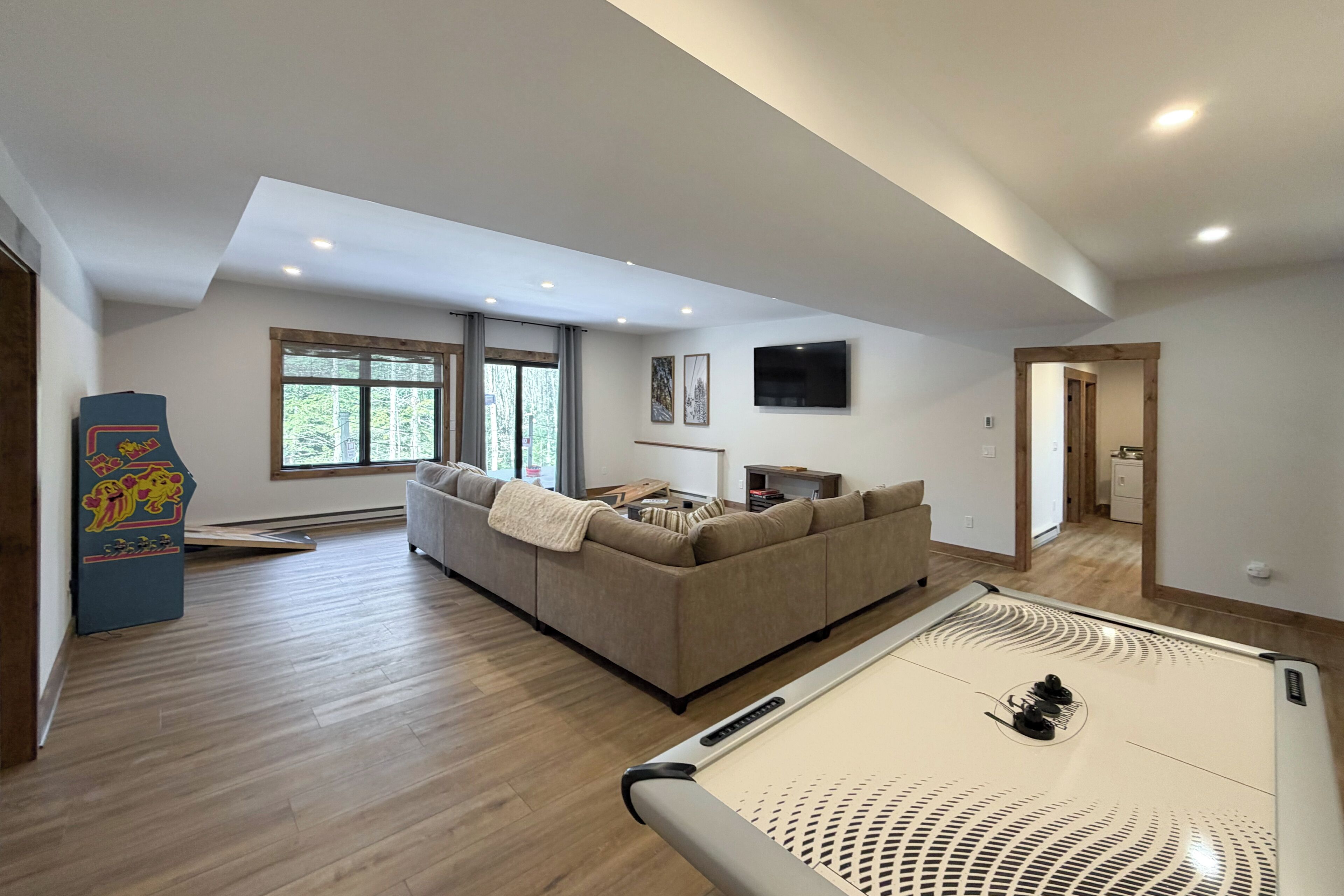 Un salón amplio con un sofá grande, una mesa de billar y un televisor montado en la pared.