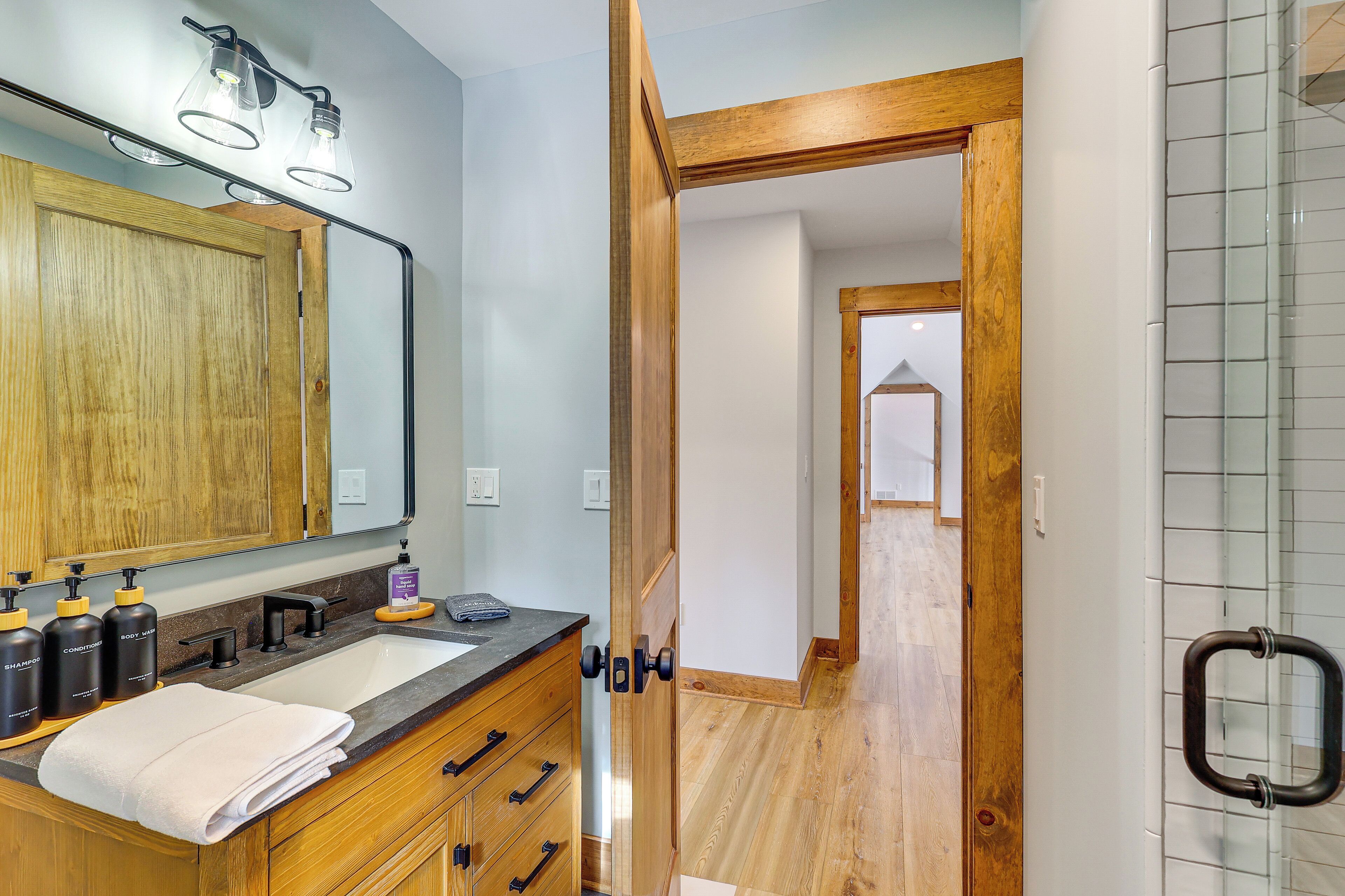 A bathroom with a wooden vanity, a large mirror, and a shower area with a glass door.