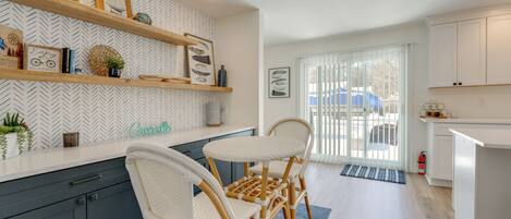 A modern kitchen with white cabinetry, wooden chairs, and decorative items on shelves.