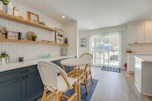 Una cocina moderna con armarios blancos, sillas de madera y adornos en las estanterías.