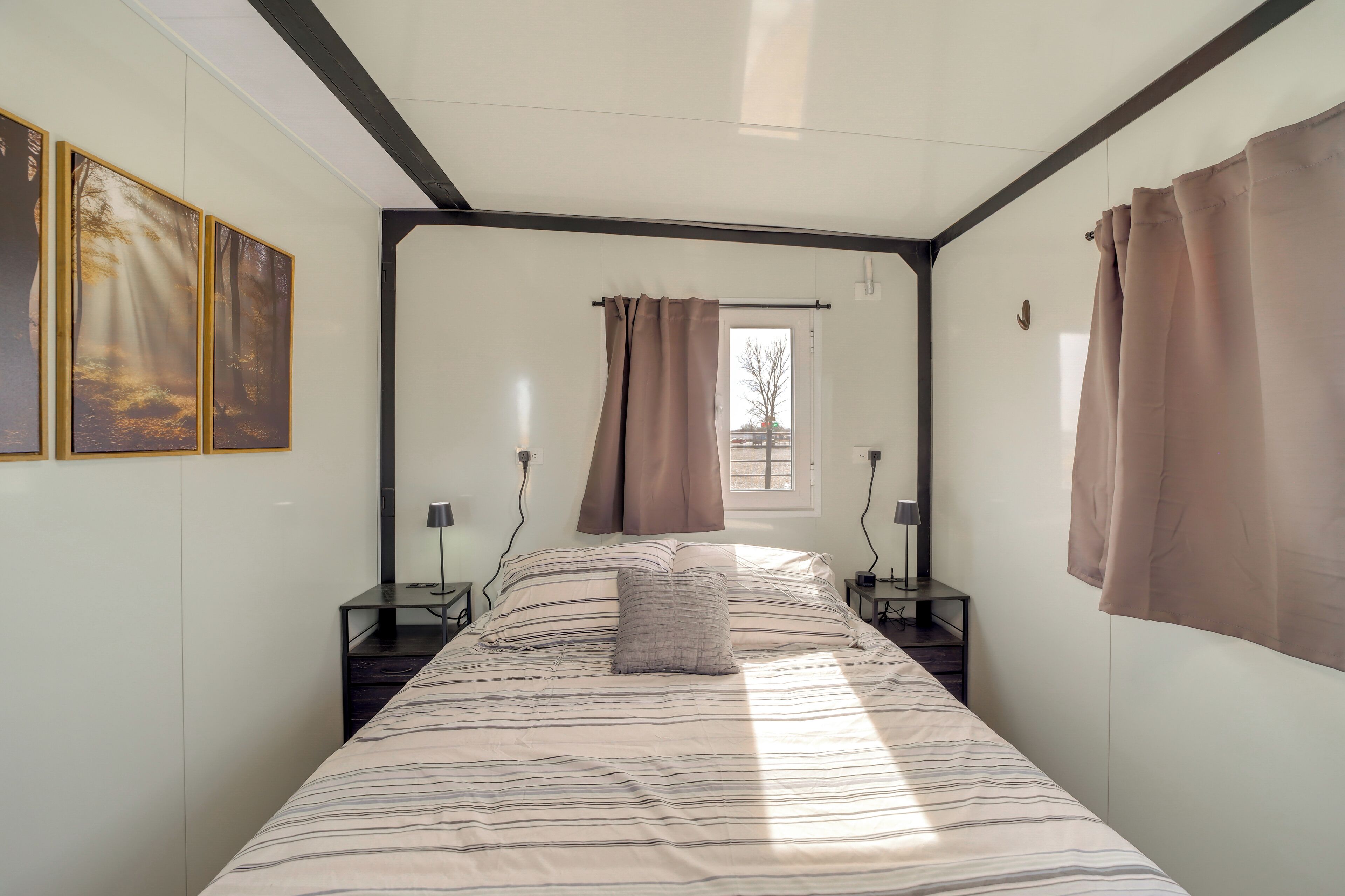 Quarto com cama grande, janela com cortinas, abajures e obras de arte na parede.