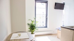 Une petite cuisine avec une fenêtre, une table avec un set de table et un verre, et une plante en pot.