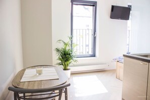 Una cocina pequeña con ventana, una mesa con camino de mesa y un vaso, y una planta en maceta.