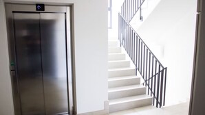 Un ascenseur moderne doté d’une signalétique directionnelle, un escalier avec des rampes noires et un intérieur propre et blanc.