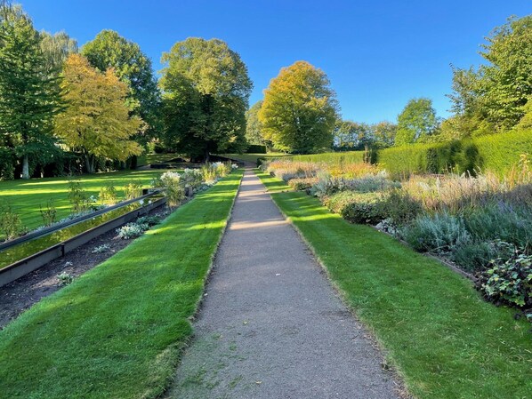 A garden pathway with a central path flanked by neatly trimmed grass and various plants.