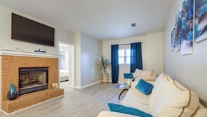 A living room with a fireplace, a sofa, a TV mounted above the fireplace, and a window with curtains. - Artistic Escape in Fayetteville! Cozy Couple's Apt (Fayetteville)
