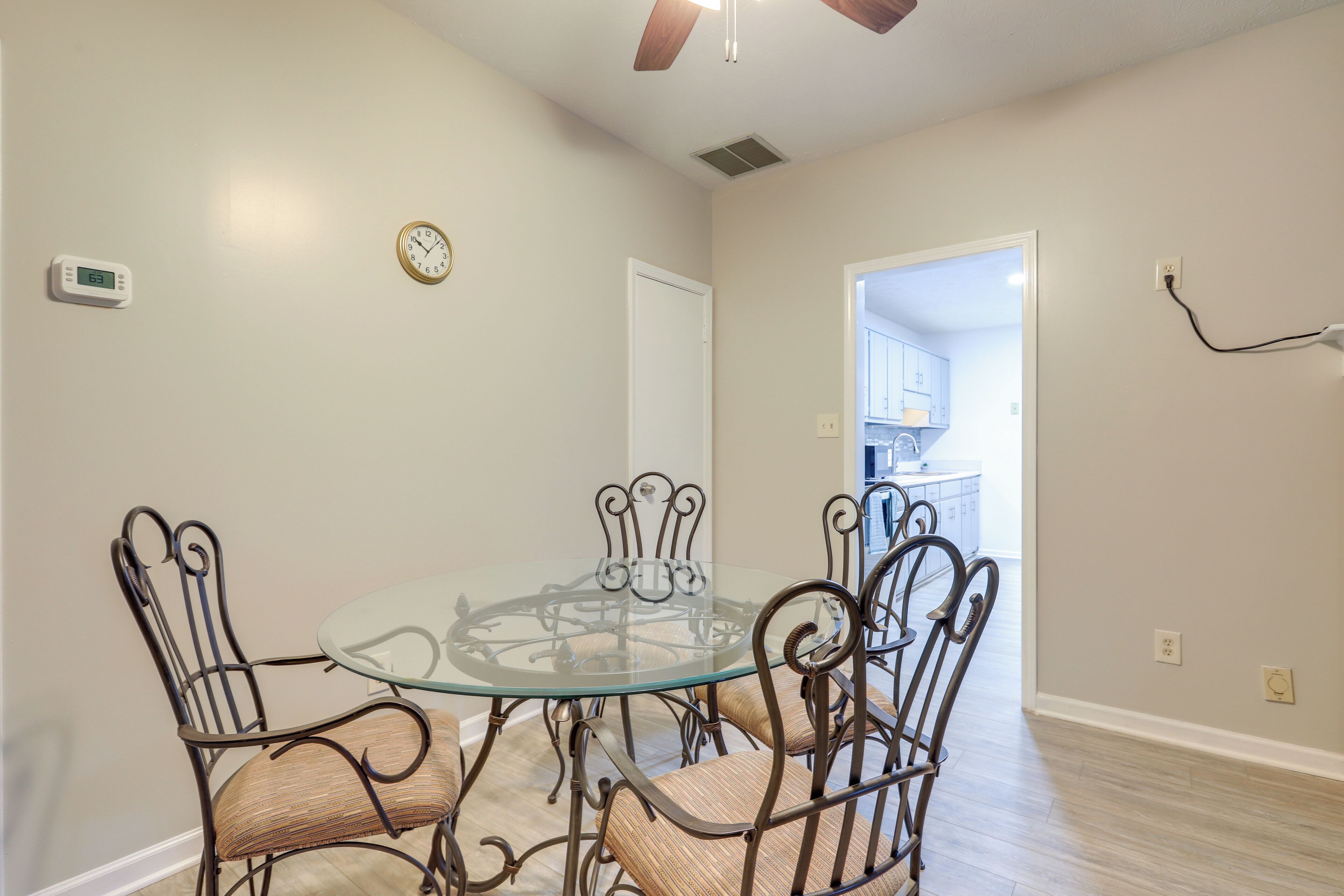 A dining area with a glass table and metal chairs, a ceiling fan, and a clock on the wall.
