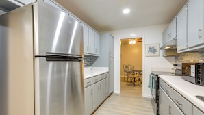 A modern kitchen with stainless steel appliances, light-colored cabinets, and a wooden dining area. - Artistic Escape in Fayetteville! Cozy Couple's Apt (Fayetteville)