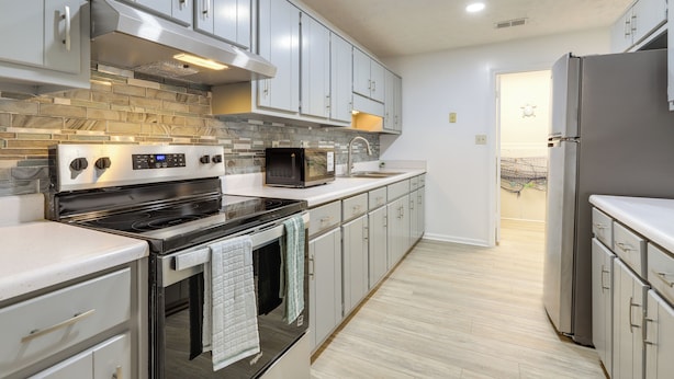 A modern kitchen with stainless steel appliances, grey cabinets, and a tiled backsplash. - Artistic Escape in Fayetteville! Cozy Couple's Apt (Fayetteville)