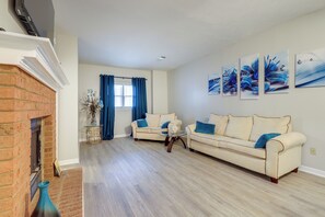 Ein Wohnzimmer mit zwei hellbeigen Sofas, einem Kamin aus Backsteinen und einer blauen Vase.
