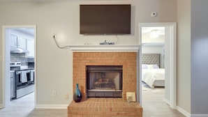 A living room with a brick fireplace, a flat-screen TV mounted above it, and a vase on the mantel. - Artistic Escape in Fayetteville! Cozy Couple's Apt (Fayetteville)